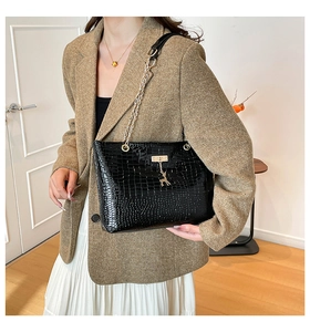 Detail of black crocodile texture bag featuring gold chain and deer charm on crossbody strap