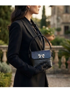 Detail of black faux crocodile leather handbag with silver bow buckle on outdoor street background