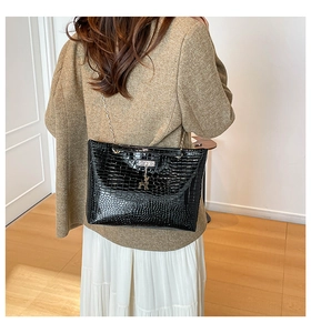 Detail view of black crocodile pattern bag with gold chain and deer charm on a model