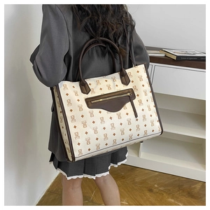 Detail view of a large cream tote bag with bear print and decorative front zipper pocket