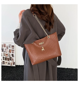 Detail of vintage brown tote bag with woven texture and gold deer pendant on chain strap