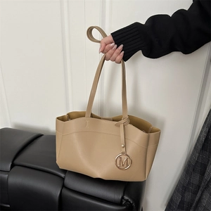 Chic beige leather tote bag with gold M charm held by model against a white wall