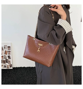 Detail of a brown woven tote bag with a golden deer charm and chain strap on a model
