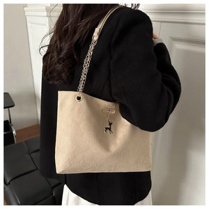 Détail du sac cabas beige avec chaîne dorée et breloque cerf porté par un mannequin