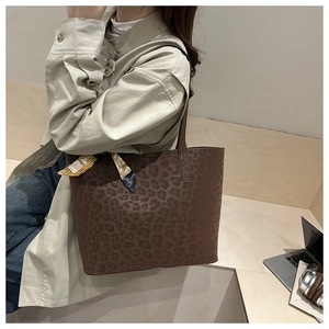 Detail of leopard print tote bag featuring a decorative silk scarf on the long handle