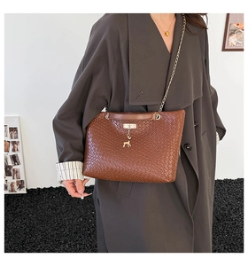 Detail of dark brown woven leather tote with gold chain strap and deer charm