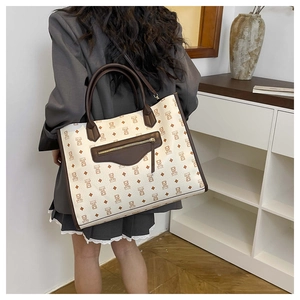 Detailed view of cream tote bag with bear pattern and brown trim worn on shoulder