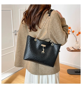 Close-up of black woven tote bag with gold deer charm and chain strap detail