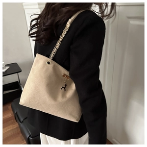 Détail du sac beige avec bandoulière chaîne dorée et pendentif cerf sur un blazer
