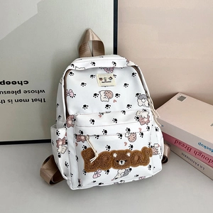 Detail shot of the cute white school bag featuring pink bows and a plush Bear patch
