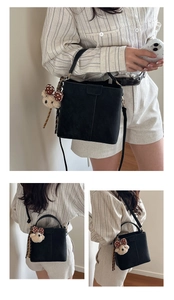 Detail view of black suede bucket bag with plush bear charm and detachable strap