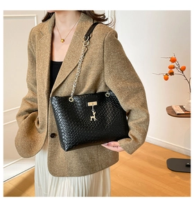 Close-up of black woven leather tote featuring gold chain strap and deer pendant charm