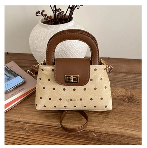 Detailed view of beige canvas polka dot bag with brown leather flap and golden twist lock