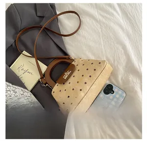 Close-up of beige polka dot handbag with brown leather strap and gold metal twist lock
