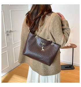 Detail of dark brown woven tote bag with chain strap and golden deer pendant decoration