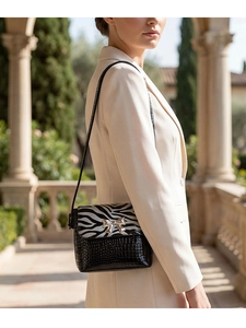 Detail of zebra print flap and golden bow hardware on a black croc-texture crossbody bag
