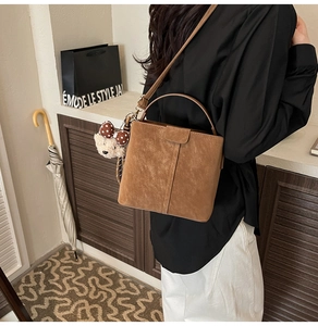 Detail of a brown suede bucket bag with a cute bear pendant and polka dot bow accessory