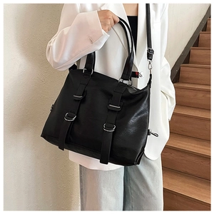 Detail of black PU leather tote bag with parallel buckles worn with a white blazer