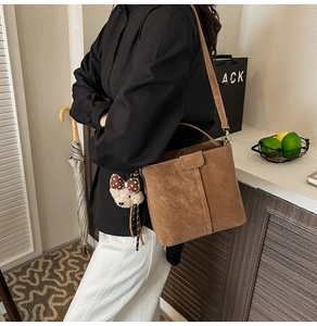 Detail of brown suede bucket bag featuring contrast stitching and a cute bear charm