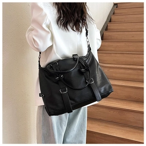 Detailed view of large black pebbled PU leather tote bag worn by model in urban setting