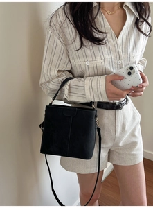 Minimalist black bucket bag shown with a long shoulder strap on a model outfit