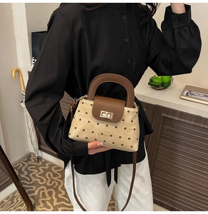 Detail view of retro polka dot handbag with brown leather handle and gold rotary lock
