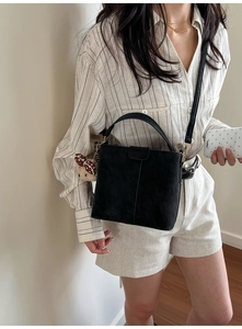 Detail of black suede bucket bag with top handle and polka dot bear charm accessory