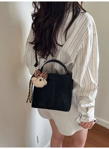 Detail of black leather bucket bag with cute plush bear charm and sleek shoulder strap