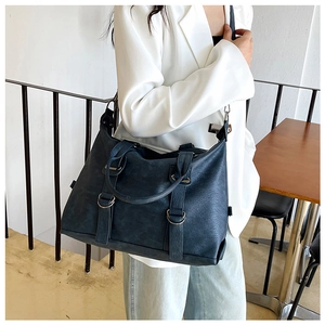 Detail of a large dark blue-grey tote bag showing grainy leather texture and metal rings