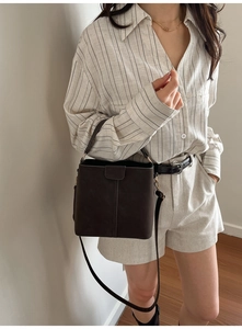 Detail of vintage matte brown bucket bag with structured flap and thin strap on a model