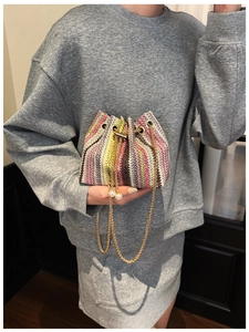 Detail of colorful woven bucket bag featuring gold chain and white pearl drawstring charms