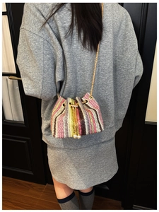Detail of colorful woven bucket bag with pearl drawstring and golden chain strap