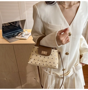 Polka dot handbag with metallic twist lock and brown handle held by a model