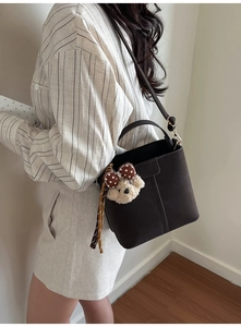 Detail of a dark brown bucket bag with a cute plush bear charm and adjustable strap