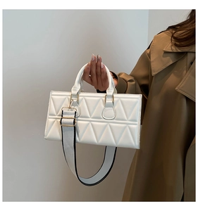 Close-up of white quilted bag with triangle patterns and wide detachable shoulder strap