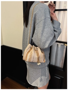 Detail of woven straw bucket bag with gold chain strap and elegant pearl drawstring