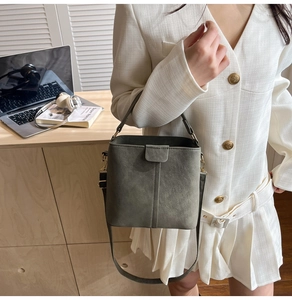 Grey-green bucket bag in matte finish held by model in a cozy office setting