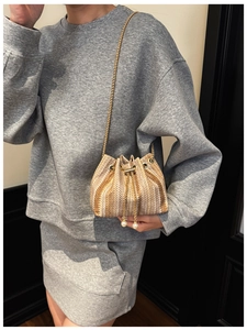 Close-up of woven bucket bag with gold chain strap and pearl drawstring tassels