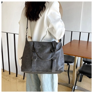 Detail of a large dark grey soft leather crossbody bag shown on a model in a cafe setting
