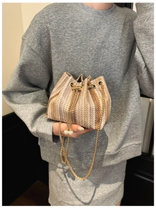Detail of woven straw bucket bag with gold chain strap and pearl drawstring charms