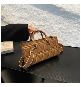 Detail of brown quilted faux leather handbag featuring a wide woven strap and gold hardware