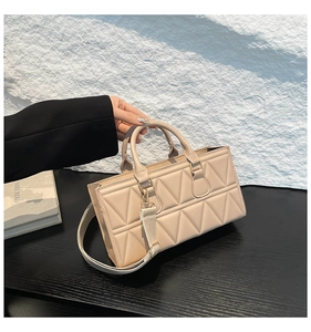 Detail of beige quilted handbag with wide strap and shiny gold-tone hardware