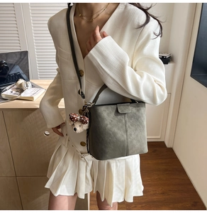 Detail of grey suede bucket bag featuring a cute teddy bear charm and brown strap