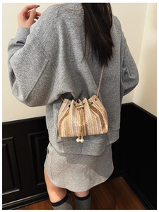 Detail of woven bucket bag with pearl drawstring charms and gold chain shoulder strap