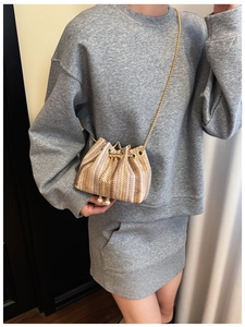 Detail view of woven bucket bag featuring wave texture, metal chain, and pearl charms