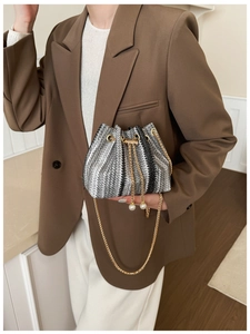 Detail of woven bucket bag with gold chain strap and elegant pearl charm accents