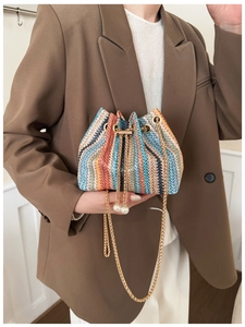 Detail of colorful woven bucket bag featuring gold chain strap and elegant pearl charm