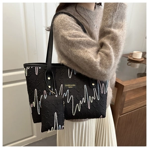 Nahaufnahme der schwarzen Tragetasche mit Wellenstickerei und kleiner Tasche im Lifestyle