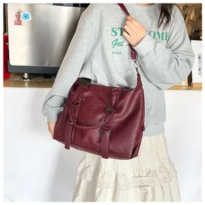 Close-up of wine red PU leather handbag with wide strap and metallic rings decoration
