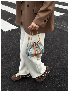 Close-up of rainbow woven bucket bag with pearl pendant and golden chain strap detail